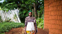A woman with a green hat poses for a photo outside a home in Burundi.