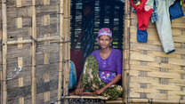 A woman sits in the doorway of her home in Myanmar and poses for a photo.
