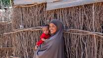 A mother holds her child in her arms outside of their home in Kenya.