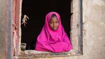 A girl in a pink outfit leans out of a windowsill in Niger.