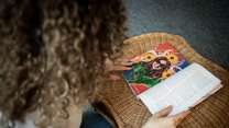 Eine Person mit lockigem Haar sitzt an einem Tisch und blättert in einem Buch