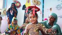 A child at an IRC Safe Spaces program in Ethiopia smiles while participating in exercise with her mother.