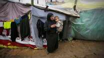 A mother holds her son in her arms outside their shelter in Gaza.