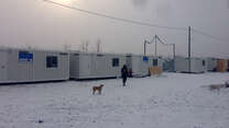 An IRc aid worker in a parka walks toward refugee shelters in Alexandria in the snow.