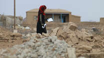 A woman picks her way through the rubble of her village in Northeast Syria.