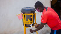 Man in red top  using an IRC water station to wash his hand