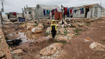 A Syrian boy walks across muddy ground amid tents in Idlib