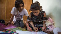 Two Yazidi sisters in Sinjar, Iraq sit on the floor of their home, coloring