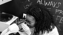 Torbertha Torbor, a nurse practitioner, looks into a microscope