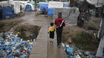 A child and a toddler walk across a wooden bridge in Moria refugee reception center, Greece.