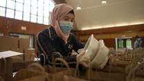 Rania Abou, wearing a mask, puts two containers of food inside paper bags to be given away as part of her work with the IRC and World Central Kitchen.