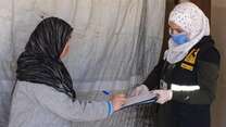 A Syrian refugee woman in Labanon signs a form to get cash assistance presented by an IRC staff member wearing PPE.