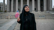 Maha al-Obaidi stands in front of a government building holding an American flag.