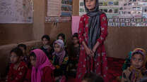 A young girl stands to speak, hands clasped, in a classroom in Afghanistan.