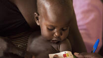 A MUAC tape around a South Sudanese baby's upper arm shows that he is at risk of acute malnutrition