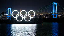 Night view of illumiated Monument of Olympic Rings, set on a barge in Tokyo with a bridge behind it