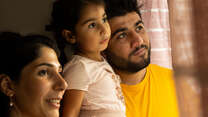 HIba and Maason, Syrian-Kurdish refugees in England, look out a window with their 4-tear-old daughter Nasrin.