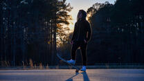 Against a forest sunset, Belqisa stands on her skateboard