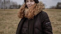 A close up of Anastasiia standing in a field wearing winter clothes