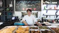 An Afghan chef smiles as he stands near trays of food at his resturant in Virginia