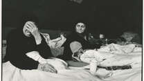 Two Bosnian women lie in beds in a refugee camp in Croatia, one of whom is crying.