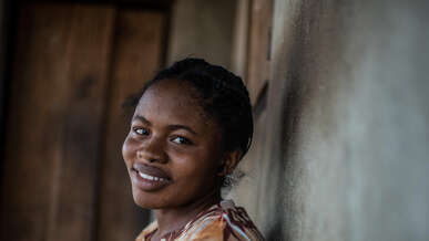 A woman stands against a wall and smiles.