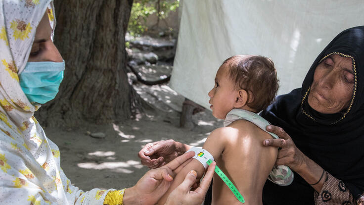 Riaz Bibi holds one of her young grandchildren. The child looks on as a nutrition counselor measures the circumference of his arm.