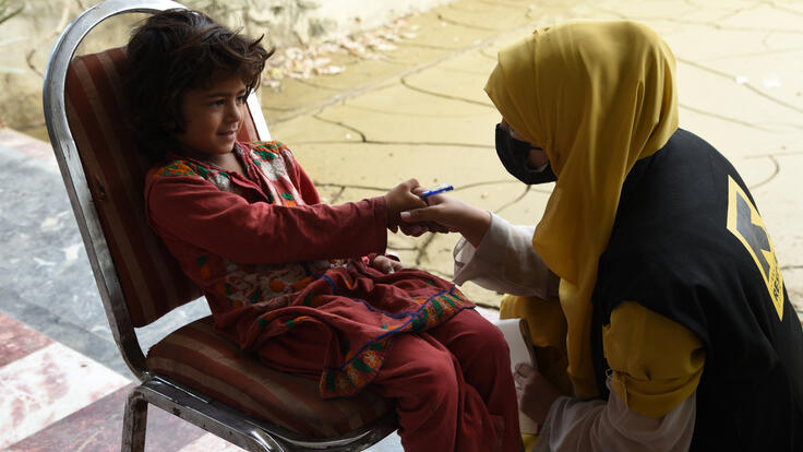 An IRC staff member shakes the hand of a young girl sitting in a chair.