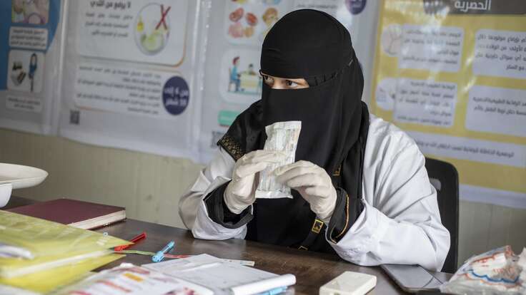 Eine Frau in einem schwarzen Niqab und medizinischem Kittel untersucht ein Dokument oder Bild in einem Büro.