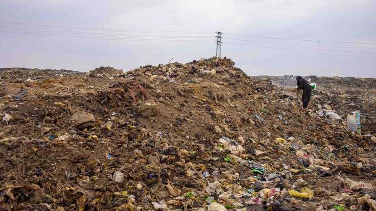 Eine riesiges Müllfeld auf dem eine Frau Müll sammelt.