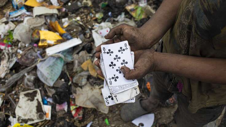 Ein Kind hält eine Spielkarte die es im Müll gefunden hat.