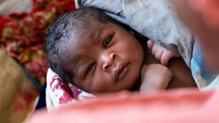 Nyfödd bebis i Tchad tittar upp mot sin mamma som håller om honom.