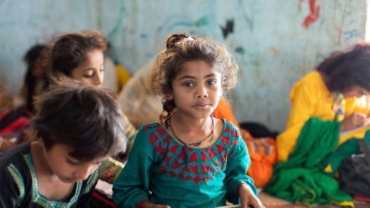 En flicka i Pakistan sitter i ett klassrum och tittar in i kameran.