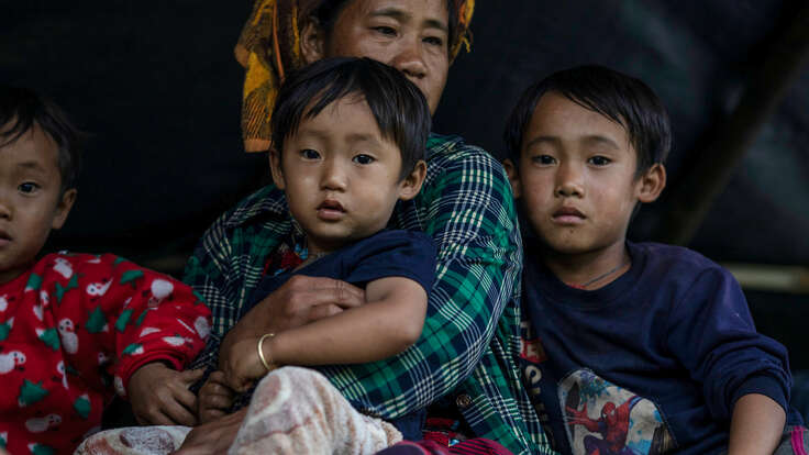 A woman holding a child and surrounded by two children looking into the camera