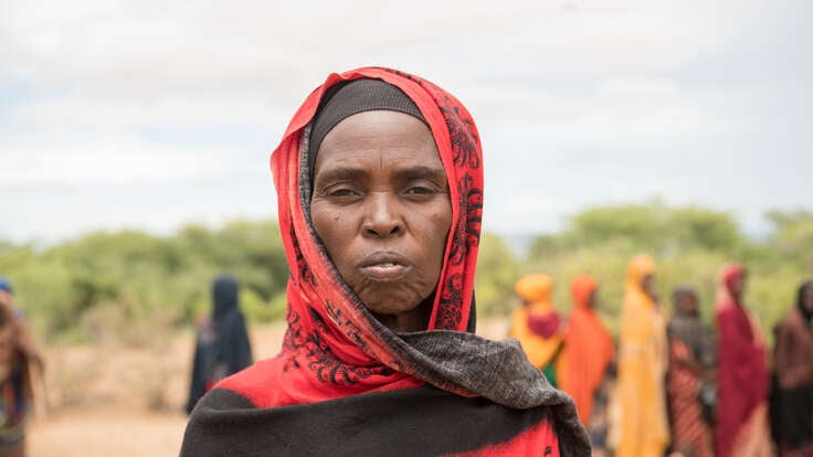 En kvinna i Etiopien tittar in i kameran. I bakgrunden syns ett flyktingläger, dit hon och hennes familj flytt efter att de drabbats av både torka och översvämningar.