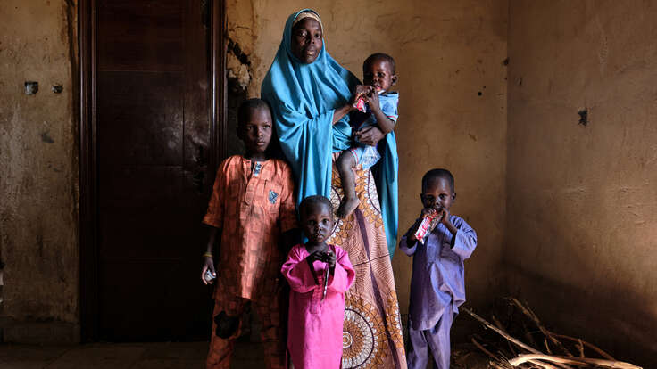 En mamma och fyra barn poserar framför kameran inomhus. Två av barnen håller i nötkräm som är en behandling mot undernäring. 
