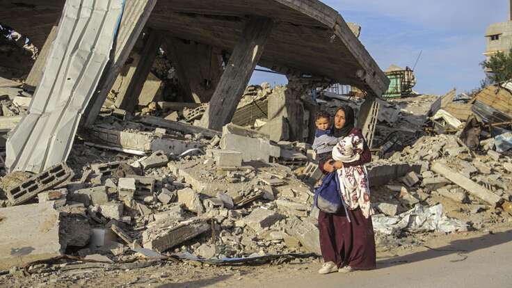 A woman holds a young child in her arms as she walks through a Palestinian community, destroyed by the war.