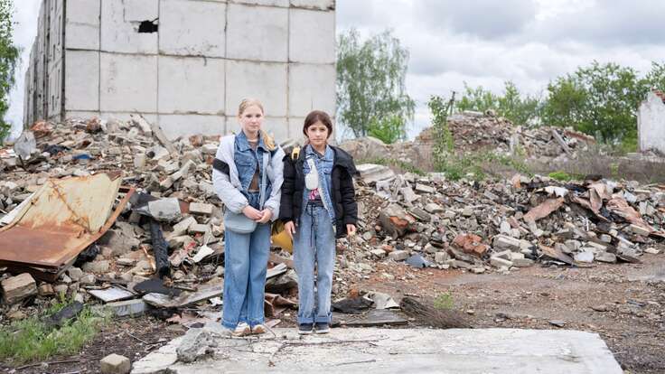 Two Ukrainian children stand in front of bombed structure.