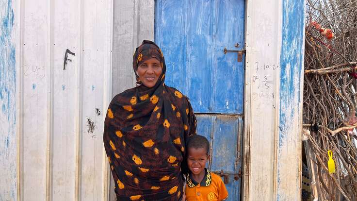 Eine Frau steht mit ihrem Kind vor einer blauen Tür.