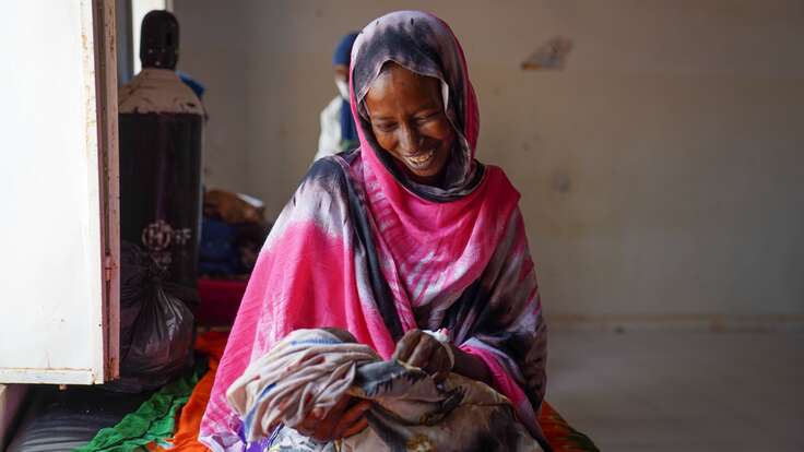 Lächelnde somalische Frau in buntem Tuch hält ein Baby im Arm.