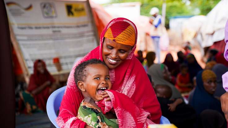 Lachende somalische Mutter hält ihr fröhliches Kind auf dem Schoß in einer Notunterkunft.