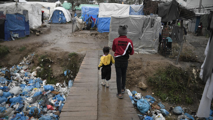A child and a toddler walk across a bridge in Moria refugee camp