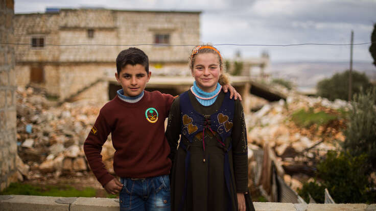 Aisha and Ali smile and pose outside their home. Ali has her arm around his sister.
