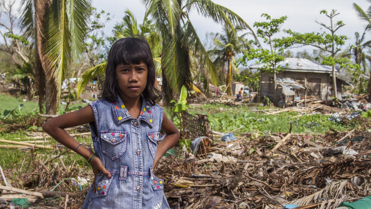 Small child standing in front a damaged home in the seaside village of Agdaliran.