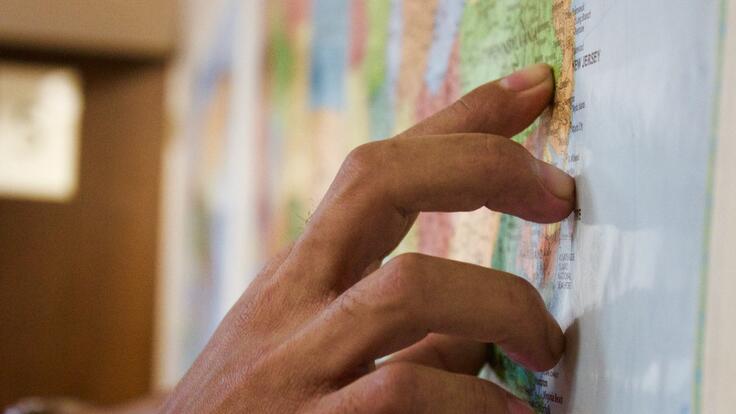 A hand pointing the the United States on a map.